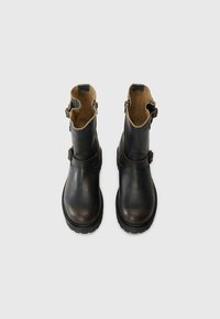 Botas de tobillo de cuero negro con punta redondeada, hebillas a los lados, forro interior acolchado color tostado y suelas de goma texturizadas.