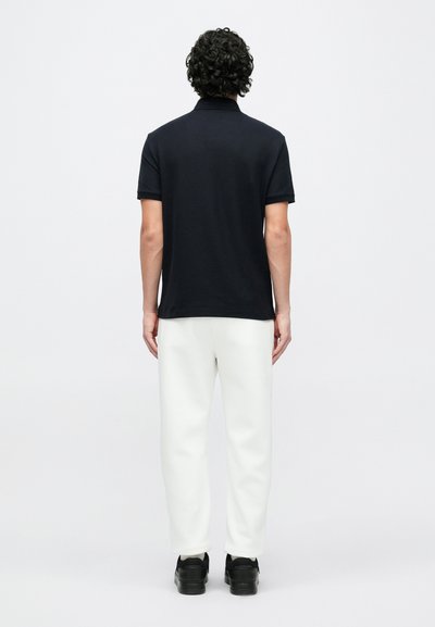 Čierne polo tričko s krátkymi rukávmi, textúrovanou látkou a klasickým golierom, v kombinácii s bielymi nohavicami a čiernymi teniskami. Viditeľný zadný pohľad.