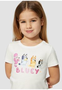 Witte katoenen t-shirt met kleurrijke tekenfilmfiguren op de voorkant en het woord "BLUEY" in vetgedrukte, pastelachtige letters.