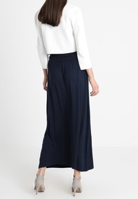Granatowa długa spódnica maxi z miękkiego, lejącego się materiału, z wysokim stanem i luźnym krojem. Połączona z białą, krótką kurtką i szarymi butami na obcasie.