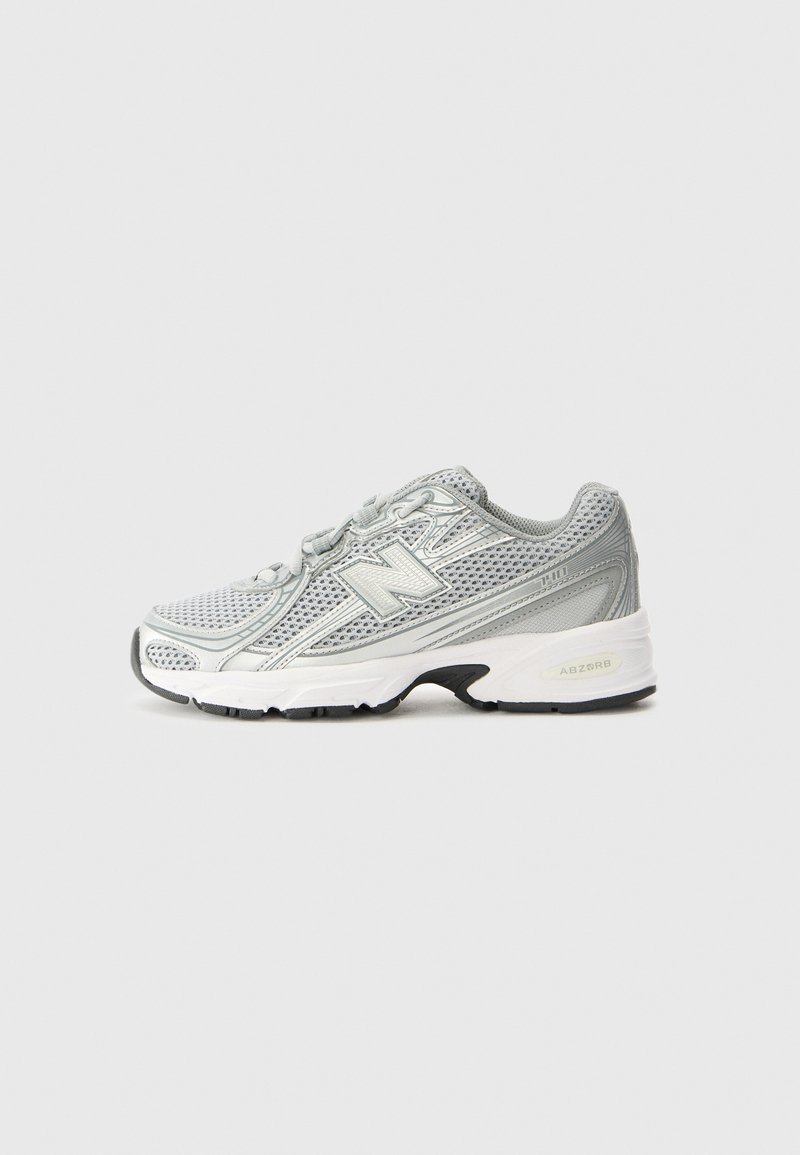 Zapatilla deportiva de color gris claro con parte superior de malla, acentos reflectantes y suela blanca acolchada. Presenta una suela exterior de goma negra y un sistema de cordones.