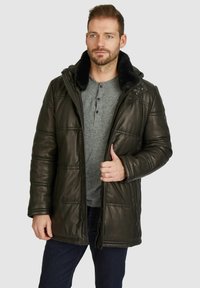 Dunkelgrüne Steppjacke mit Kunstfellkragen, mit Reißverschluss, gestepptem Design und zwei Seitentaschen, getragen über einem grauen Henley.