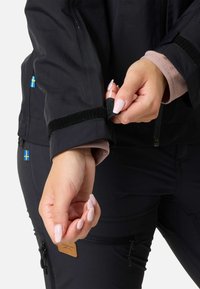 Sort udendørsjakke med velcro-manchetter, fremhævet af fleece-foring ved håndleddet. Har et lille svensk flag på ærmet.