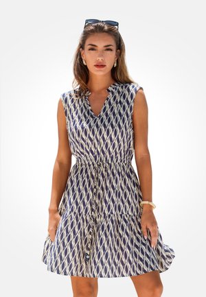 Marineblauwe en crèmekleurige jurk met patroon, V-hals, korte mouwen en een riem in de taille; heeft een gelaagde rok met een vloeiend ontwerp.