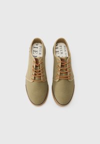 Khaki canvas shoes with brown laces, a rounded toe, and a rubber sole. Features a striped accent on the heel and printed insole.