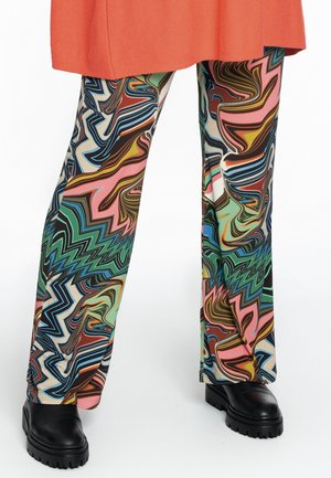 Pantalones largos con patrones abstractos de remolinos multicolores combinados con zapatos negros de plataforma gruesa y el dobladillo de un abrigo naranja.
