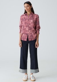 Chemise à col boutonné au motif tie-dye rose, associée à un jean en denim noir à larges jambes avec des ourlets retroussés et des sneakers blanches à rayures multicolores.