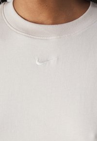 Camiseta de algodón gris claro con un cuello redondo estrecho de canalé y pequeño logotipo de Nike bordado en blanco en el pecho.