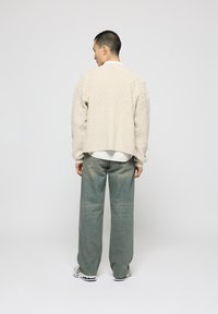 Beige strikket cardigan med diamantmønster, afslappet pasform, ribbede manchetter, parret med lysegrønne vide jeans og sneakers.