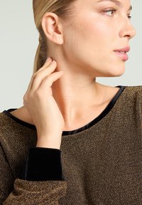 Haut en maille noir et or avec un col arrondi, doté de poignets en velours noir. Texture lisse, détails en fils réfléchissants partout.