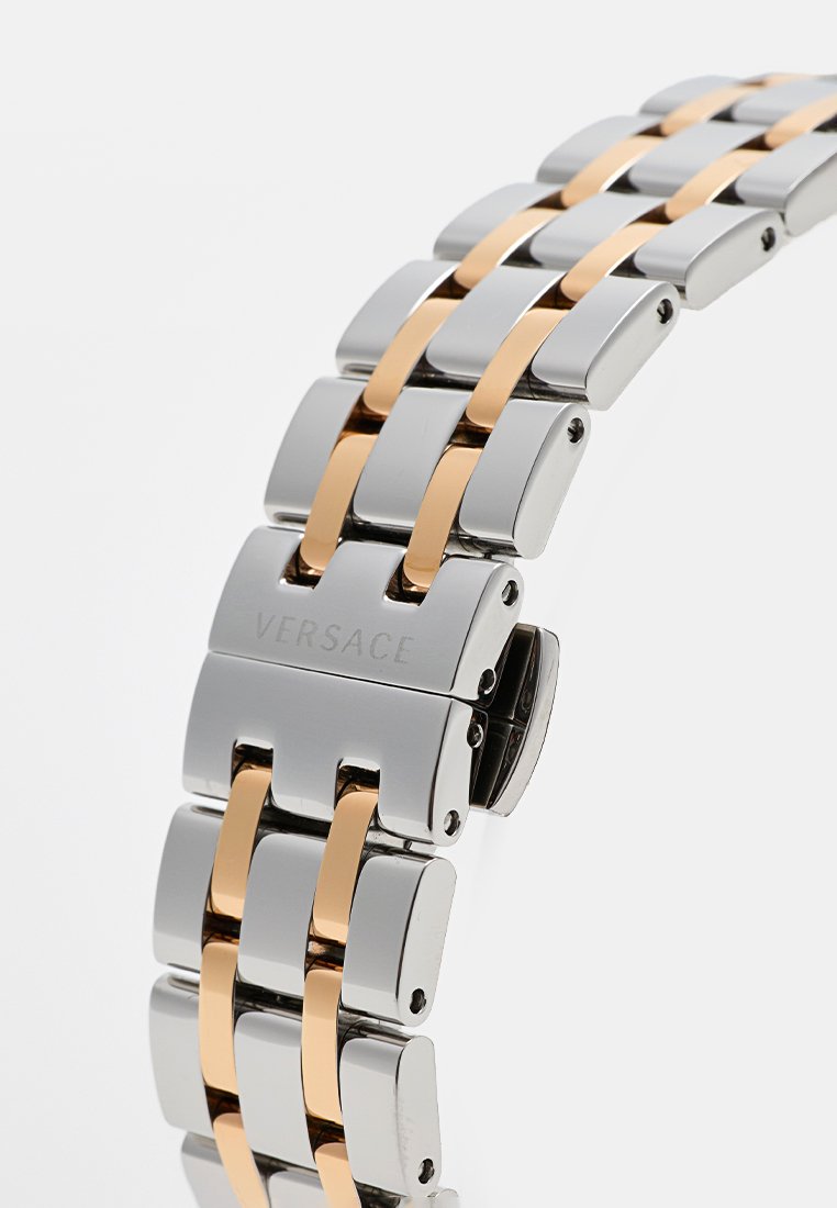 Montre Versace avec un bracelet en métal argenté et doré, avec des maillons polis et un fermoir lisse.