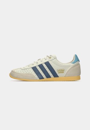 Nízkoprofilová sneaker Adidas Japan v off-white s modrými pruhy, béžovým semišovým špičkou a patou, světle modrým poutkem na patě a gumovou podrážkou.