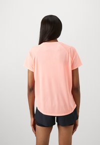 T-shirt de sport rose clair à manches courtes, en tissu texturé et avec un ourlet arrondi, associé à un short noir. Vue arrière.