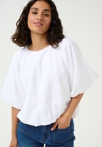 Hvid kortærmet top med rund halsudskæring, løs pasform og let tekstureret stof, parret med blå denimjeans.