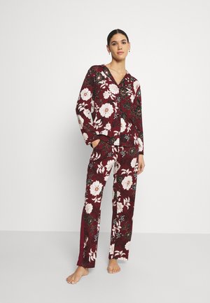 Red floral pajama set features a button-up top with long sleeves and matching pants, both adorned with white flowers and green accents.