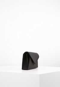 Czarna kopertówka o uporządkowanym, prostokątnym kształcie. Wykonana z gładkiego materiału, posiada zapięcie na klapkę oraz kanciastą sylwetkę.