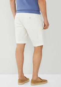 Pantaloni cargo color beige chiaro con due tasche posteriori, chiusure a bottone e risvolti, abbinati a scarpe slip-on in suede marroni.
