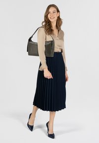 Graue Lederhandtasche mit glatter Oberfläche und strukturiertem Design, kombiniert mit einer beigefarbenen Bluse und einem marineblauen plissierten Rock.