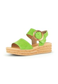 Green suede sandal with a wide front strap and an ankle strap, featuring a circular wooden buckle and a textured wedge sole.