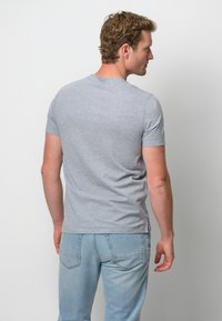 Grå bomull t-shirt med kort ärm, rund halsringning och en åtsittande design, bärs tillsammans med ljusblå jeans, visad från baksidan.