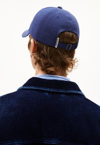 Navyblaue Baumwollmütze mit verstellbarem Riemen hinten, getragen mit einer strukturierten dunkelblauen Cordjacke.