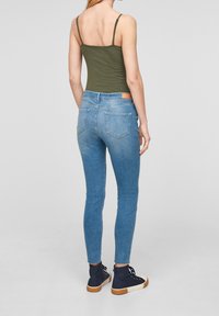 Groene tanktop, blauwe skinny jeans met een vervaagde wassing, achterzakken, bruine leren label bij de taille, gecombineerd met marineblauwe hoge sneakers.
