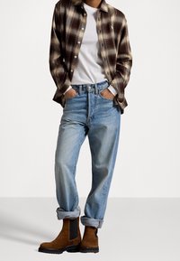 Rutig flanellskjorta i brun och beige, vit T-shirt, ljusblå denimjeans med uppkavlade byxben och bruna mockaboots med elastiska sidor.