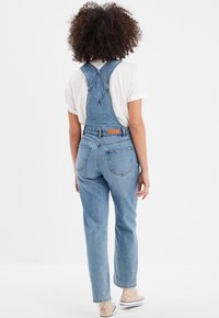Pantalones de mezclilla en azul claro con un diseño clásico, que cuentan con tirantes ajustables, un peto trasero y múltiples bolsillos. Tejido de algodón con una ligera textura.