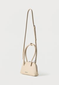 Μπεζ τσάντα χειρός από δερμάτινη υφή με δύο κοντές λαβές, ένα μακρύ, ρυθμιζόμενο ιμάντα για φοδρακιώση στον ώμο και ασημένιο φερμουάρ στο πάνω μέρος.