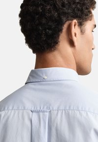 Hellblaues Hemd mit durchgehender Knopfleiste, klassischem Kragen, Rückenfalte und einem Perlmutt-Druckknopf am Hals, gefertigt aus glattem Baumwollstoff.