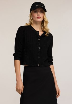 Zwarte geribbelde cardigan met een ronde halslijn en knoopsluiting, met een cropped ontwerp en subtiele glans, gecombineerd met een bijpassende zwarte pet.