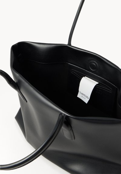 Sac cabas en cuir noir avec deux poignées, ouverture sur le dessus et une étiquette blanche à l'intérieur indiquant le nom de la marque "THEMOIRè."