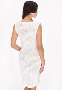 Weißes gestricktes Kleid mit einer figurbetonten Silhouette, das über ein strukturiertes Muster und seitliche Knopfakzente verfügt. Ärmelloses Design erhöht die Atmungsaktivität.