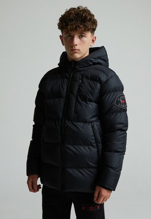 Black puffer jacket with a hood, featuring a zip closure, quilted texture, and an emblem on the left sleeve. Model wearing black pants.