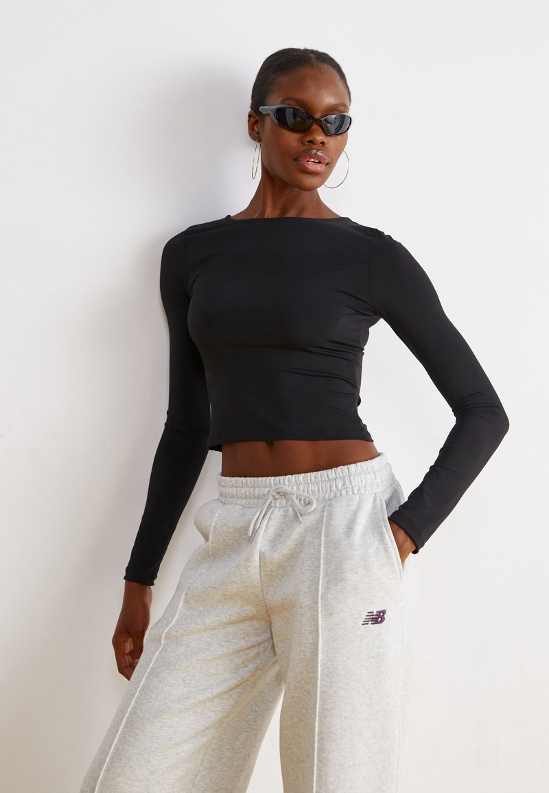 Zwarte langemouw crop top gecombineerd met lichtgrijze sweatpants. De broek heeft een paars "New Balance" logo op de bovenbeen. Gestructureerde stof.