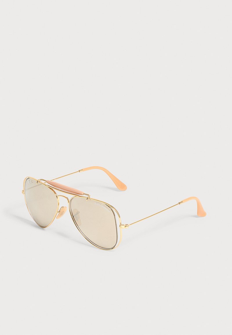 Γυαλιά ηλίου aviator με χρυσό πλαίσιο, φακούς σε ανοιχτή μπεζ απόχρωση και άκρες σκελετού ροδακινί χρώματος πάνω σε ανοιχτό φόντο.