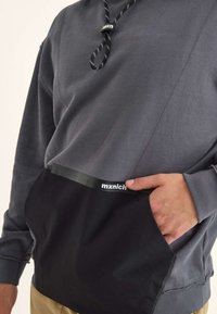 Felpa da uomo grigia con un pannello inferiore nero, dotata di tasca a marsupio e cordino regolabile sul collo. Accentuata con logo.