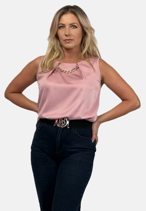 Pink satin sleeveless top with pleated detail, adorned with a gold chain accent. Worn with high-waisted dark jeans and belt featuring a metallic buckle.
