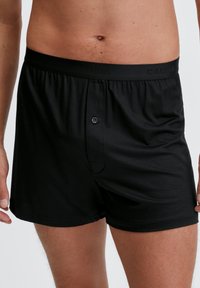 Zwarte katoenen boxershort met een elastische tailleband met "CALIDA"-branding. Voor sluiting met knoop en een gladde textuur. Lengte tot halverwege de dij.