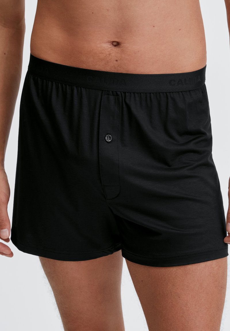 Zwarte katoenen boxershort met een elastische tailleband met "CALIDA"-branding. Voor sluiting met knoop en een gladde textuur. Lengte tot halverwege de dij.