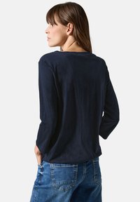Marinefarbenes Langarmoberteil aus leichtem Material, mit einer lockeren Passform und einem schlichten Rundhalsausschnitt. Getragen mit blauen Jeans.