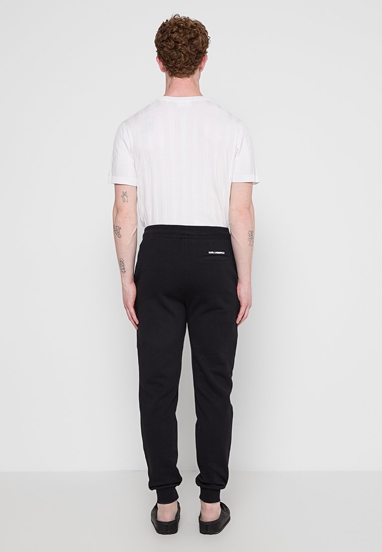 Pantaloni sportivi neri con una vestibilità comoda, vita elastica e un piccolo etichetta del marchio sul retro. Abbinati a una maglietta bianca semplice.
