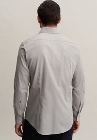 Grå långärmad skjorta med en slät textur, knäppningar vid ärmsluten och en spetsig krage. Har en skräddarsydd passform och en rundad nederkant.