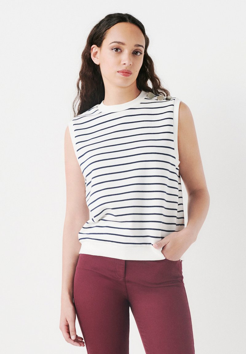 Top blanco sin mangas con rayas azul marino, escote y dobladillo acanalados. Presenta botones decorativos en un hombro. Combinado con pantalones burdeos.