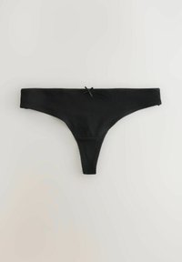 Tanga de algodón negro con pequeño lazo frontal y borde ondulado, colocado plano sobre una superficie clara.