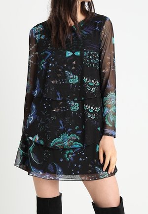 Robe longue noire transparente à manches longues avec jupe à volants présentant des motifs floraux et de papillons en turquoise, bleu et violet, portée avec des bottes noires montant jusqu'aux genoux.