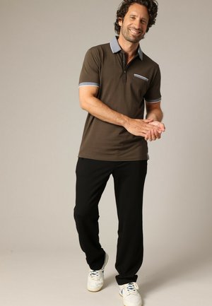 Polo marron avec un col et des poignets bleus, doté d'une poche poitrine et associé à un pantalon noir et des baskets blanches.