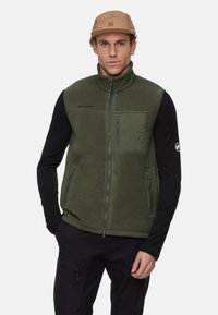 Groene fleece vest met ritszakken, hoge kraag en Mammut-logo. Draag het over een zwarte langemouwen shirt, heeft een gestructureerd oppervlak.