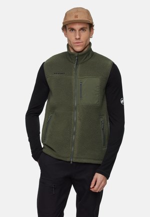 Green fleece vest with zippered pockets, high collar, and Mammut logo. Worn over a black long-sleeve shirt, features a textured surface.