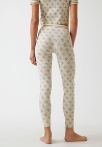 Obcisłe, kremowe legginsy z wzorem brązowych logo i wysokim stanem, zestawione z pasującą koszulką z krótkim rękawem.